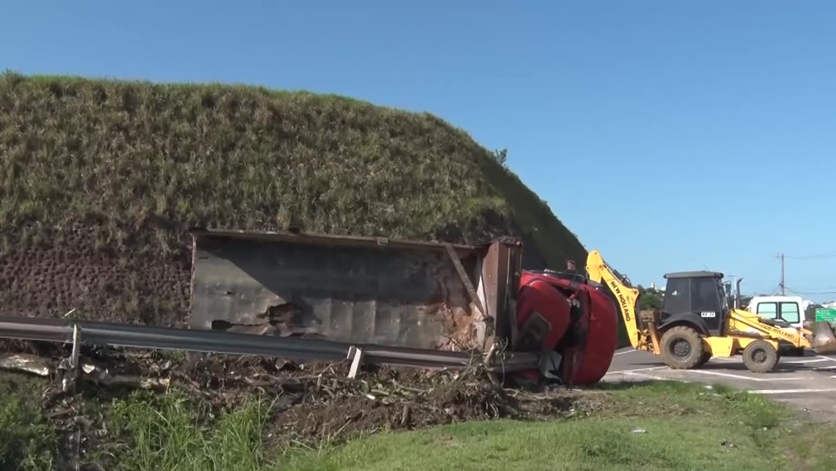 Caminhão caçamba tombado ao lado do guard-rail, no trevo de Meaípe