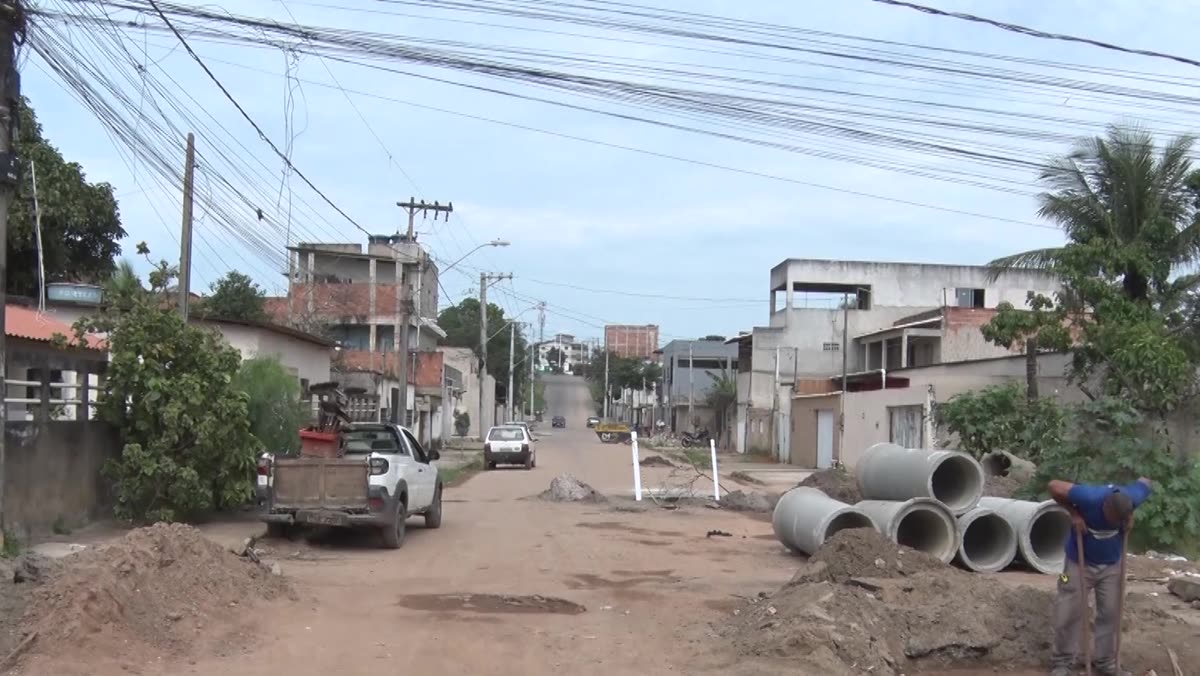 Rua de terra com manilhas e equipe trabalhando na obra de drenagem