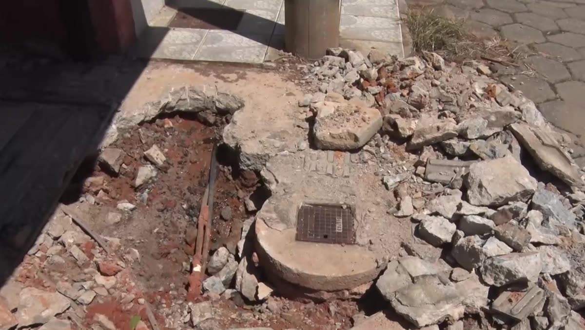 Buraco aberto na calçada, com tampa de caixa e entulho ao redor