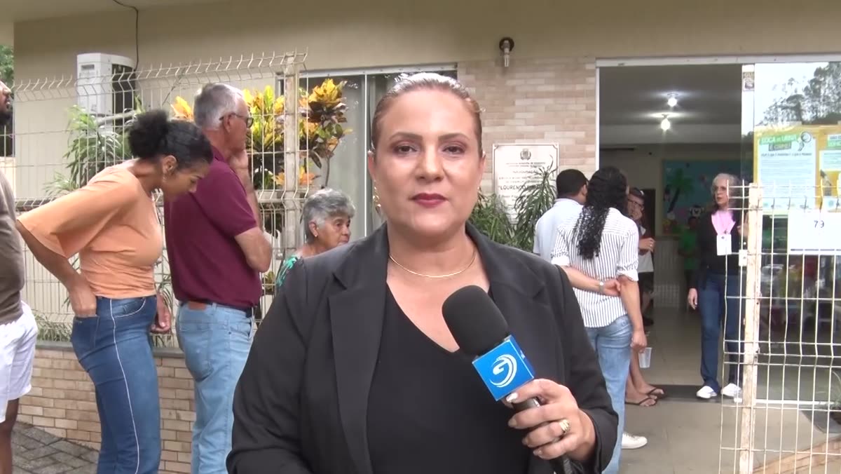 Repórter da TV Guarapari em frente a um local de votação, com eleitores ao fundo