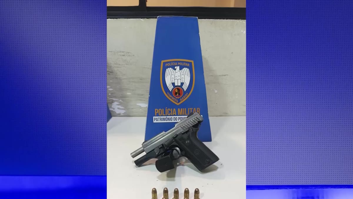 Pistola e munições apreendidas, sobre uma bancada ao lado de um suporte da Polícia Militar